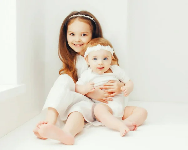 Two Cute Older Younger Sisters Children Hugging Together Home White — Stock Photo, Image