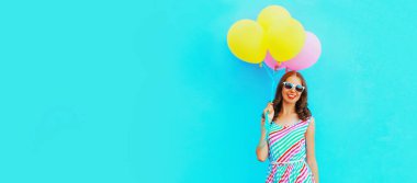 Mavi arka planda renkli bir elbise giyen ve bir sürü balonu olan mutlu, güzel bir genç kadının portresi.