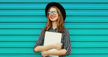 Mutlu gülümseyen genç bir kadının portresi dizüstü bilgisayarını tutuyor, uzaklara bakıyor mavi arka planda hayal kuruyor.