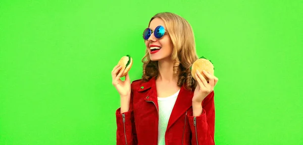 スタイリッシュな幸せな笑顔の若い女性の肖像緑のカラフルな背景においしい大きなハンバーガーのファーストフードを食べる — ストック写真