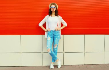 Şehir caddesinde kırmızı arka planda günlük, yaz hasır şapkası takan genç bir kadın model.