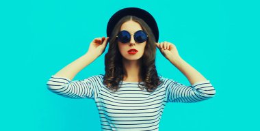 Çizgili tişört ve mavi arka planda yaz hasır şapkası giyen şık genç kadın modelin portresi.