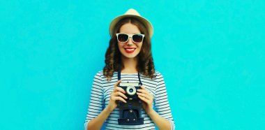 Mutlu gülümseyen genç kadın fotoğrafçının renkli mavi arka planda klasik film kamerasıyla yaz portresi.