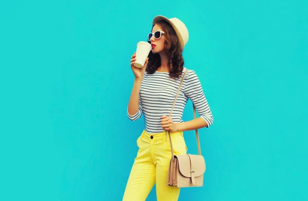 青を基調としたハンドバッグ 縞模様のTシャツ 夏の麦藁帽子をかぶったカップからコーヒーを飲むスタイリッシュな若い女性の肖像画 — ストック写真