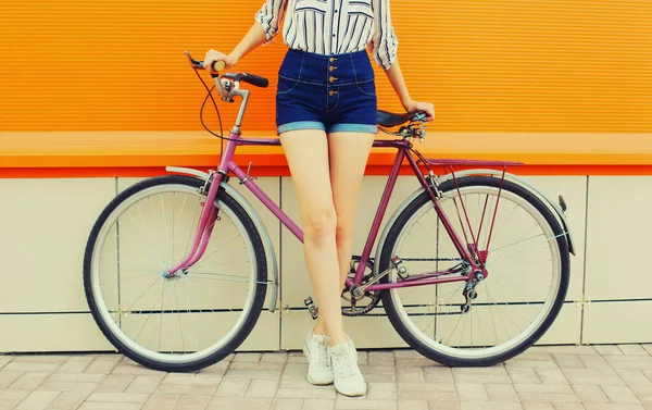 城市里穿着短裤 骑自行车 背著橙色背景的年轻漂亮女子的腿的夏季画像 — 图库照片