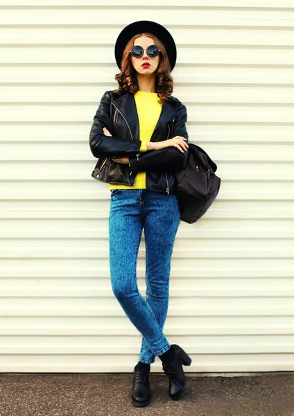 黒のロックスタイルのジャケット 黄色のセーター 白い背景にバックパックを身に着けているポーズスタイリッシュな若い女性モデルのファッショナブルな肖像画 — ストック写真