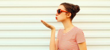 Havalı genç bir kadının portresi dudaklarını siliyor kırmızı rujlu tatlı bir öpücük beyaz arka planda havalı saç stili olan çizgili bir tişört giyiyor.