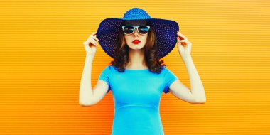 Portrait of beautiful young woman wearing a summer hat and dress on city street over orange background