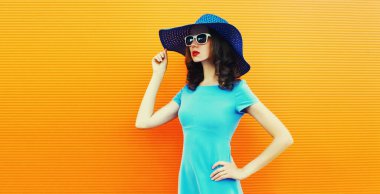 Portrait of beautiful young woman wearing a summer hat and dress on city street over orange background