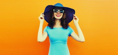 Portrait of beautiful happy smiling young woman wearing a summer hat and dress on city street over orange background