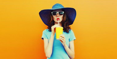 Colorful portrait of beautiful young woman drinking a fresh juice wearing a summer hat an orange background