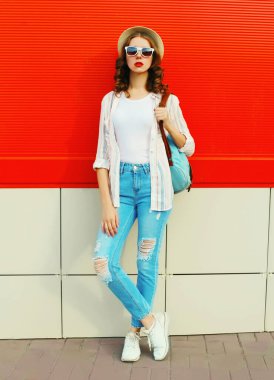 Şehir caddesinde kırmızı arka planda günlük, yaz hasır şapkası takan genç bir kadın model.