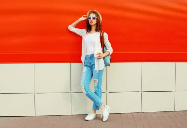 Şehir caddesinde kırmızı arka planda günlük, yaz hasır şapkası takan genç bir kadın model.