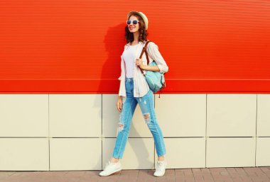 Şehir caddesinde kırmızı arka planda günlük, yaz hasır şapkası takan genç bir kadın model.