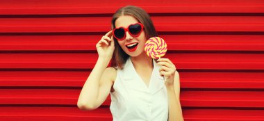 Kırmızı arka planda lolipopu olan mutlu, genç bir kadının yaz portresi.