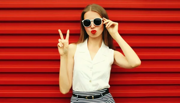スタイリッシュな若い女性モデルのポージング彼女の唇とともに赤い口紅身に着けているサングラス赤の背景 — ストック写真