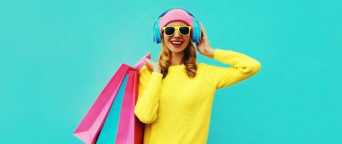 Kulaklıkla müzik dinleyen, sarı örgü süveter, mavi arka planda pembe şapka giymiş, kulaklık takan, şık bir genç kadının renkli portresi.
