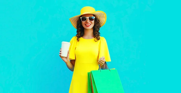 青い背景に黄色の夏のわら帽子を身に着けているショッピングバッグと美しい幸せな笑顔の女性の肖像画 — ストック写真