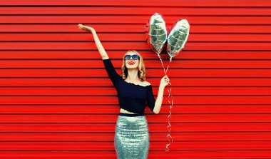 Kırmızı arka planda gümüş kalp şeklinde balonları olan güzel, mutlu, genç bir kadının portresi.