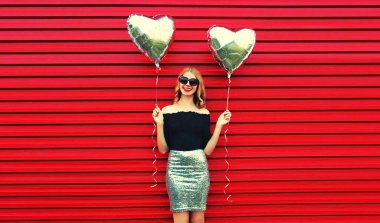 Kırmızı arka planda gümüş kalp şeklinde balonları olan güzel, mutlu, genç bir kadının portresi.