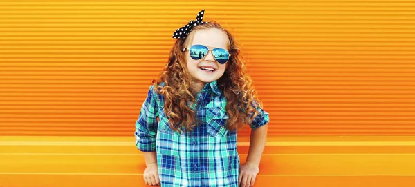 Portrét Malé Kudrnaté Holčičky Kostkované Košili Sluneční Brýle Oranžovém Pozadí — Stock fotografie
