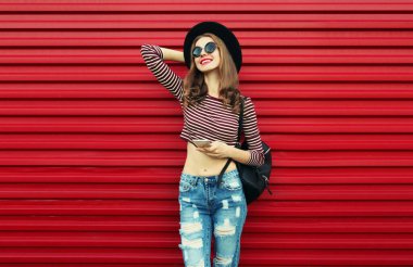 Kırmızı arka planda siyah yuvarlak bir şapka takan zarif, gülümseyen genç bir kadının portresi.