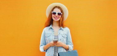 Şehirde telefon ve alışveriş çantalarıyla turuncu bir geçmişi olan modern bir genç kadın.