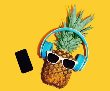 Kablosuz kulaklıkla sarı arka planda telefonla müzik dinleyen şık ananaslı renkli bir görüntü.