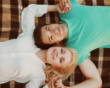 Mutlu genç bir çiftin portresi. Ekoseli bir manzarada yan yana yatıyorlar.