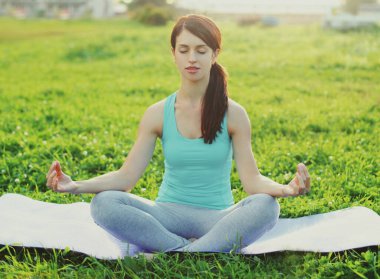 Spor salonundaki kadın güneşli yaz parkında çimlerde yoga egzersizleri yapıyor.