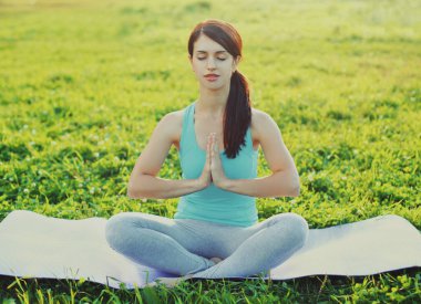 Spor salonundaki kadın güneşli yaz parkında çimlerde yoga egzersizleri yapıyor.