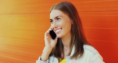 Portakal rengi arka planda telefonla arayan gülümseyen genç bir kadının portresi.