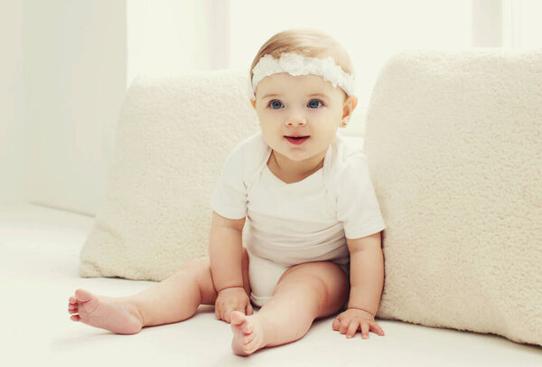 Portrait of cute little baby sitting in white room at home near window