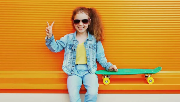陽気な笑いの女の子の子供の肖像 オレンジ色の背景に市内でスケートボードとポーズ — ストック写真