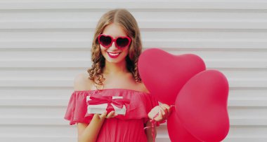 Mutlu gülümseyen kadın portresi hediye kutusu ve beyaz arka planda pembe kalp şeklinde balon.