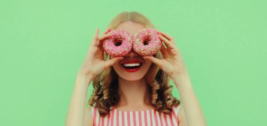 Yeşil arka planda eğlenen iki donutlu mutlu genç kadının portresi.