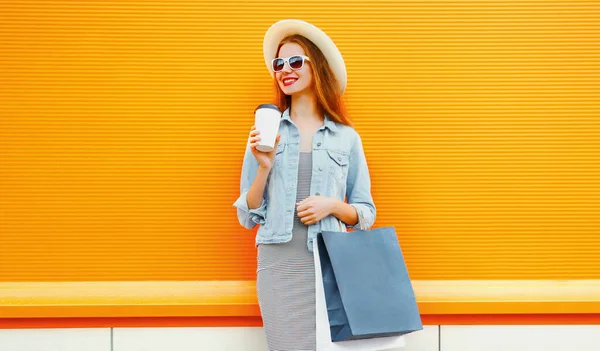 带着购物袋和咖啡杯 头戴夏草帽 头戴橙色背景的快乐年轻女性的画像 — 图库照片