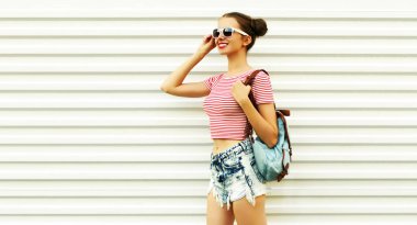 Beyaz arka planda sırt çantalı, güzel saçlı, gülümseyen genç bir kadının yaz portresi.