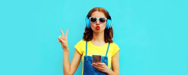 Kulaklıklı genç bir kadının portresi mavi arka planda telefonla müzik dinliyor.