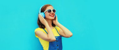 Renkli mavi arka planda kulaklıkla müzik dinleyen mutlu bir kadının portresi.