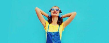 Renkli mavi arka planda kulaklıkla müzik dinleyen mutlu bir kadının portresi.