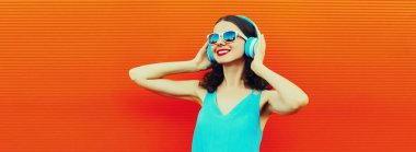 Renkli turuncu arka planda kulaklıkla müzik dinleyen mutlu bir kadının portresi.