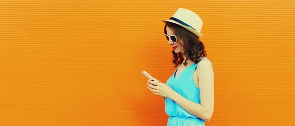 オレンジ色の背景に夏のわらの帽子を身に着けているスマートフォンと白人の若い女性の肖像画 — ストック写真