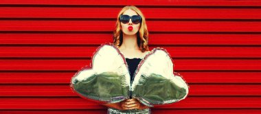 Güzel bir kadının portresi dudaklarını üflüyor ve ellerinde gümüş kalp şeklinde balonlarla tatlı bir öpücük yolluyor.