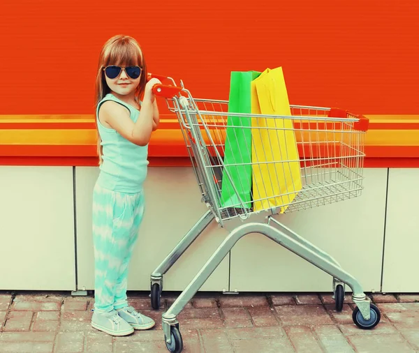 Κοριτσάκι Καρότσι Και Τσάντες Για Ψώνια Στο Δρόμο Της Πόλης — Φωτογραφία Αρχείου