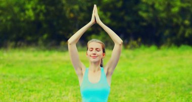 Yaz parkında çimlerin üzerinde yoga egzersizleri yapan genç bir kadın.