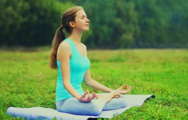 Yaz parkında çimlerin üzerinde yoga egzersizleri yapan genç bir kadın.