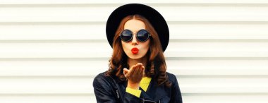 Şık bir genç kadın modelin şık portresi dudaklarını siliyor. Beyaz arka planda siyah rock tarzı ceket giyip tatlı bir öpücük yolluyor.