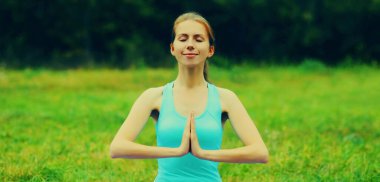 Yaz parkında çimlerin üzerinde yoga egzersizleri yapan genç bir kadın.