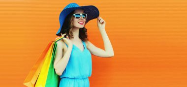 Renkli alışveriş çantaları olan, turuncu arka planda yaz hasır şapka takan, reklam metinleri için boş kopya alan güzel, mutlu genç bir kadının portresi.